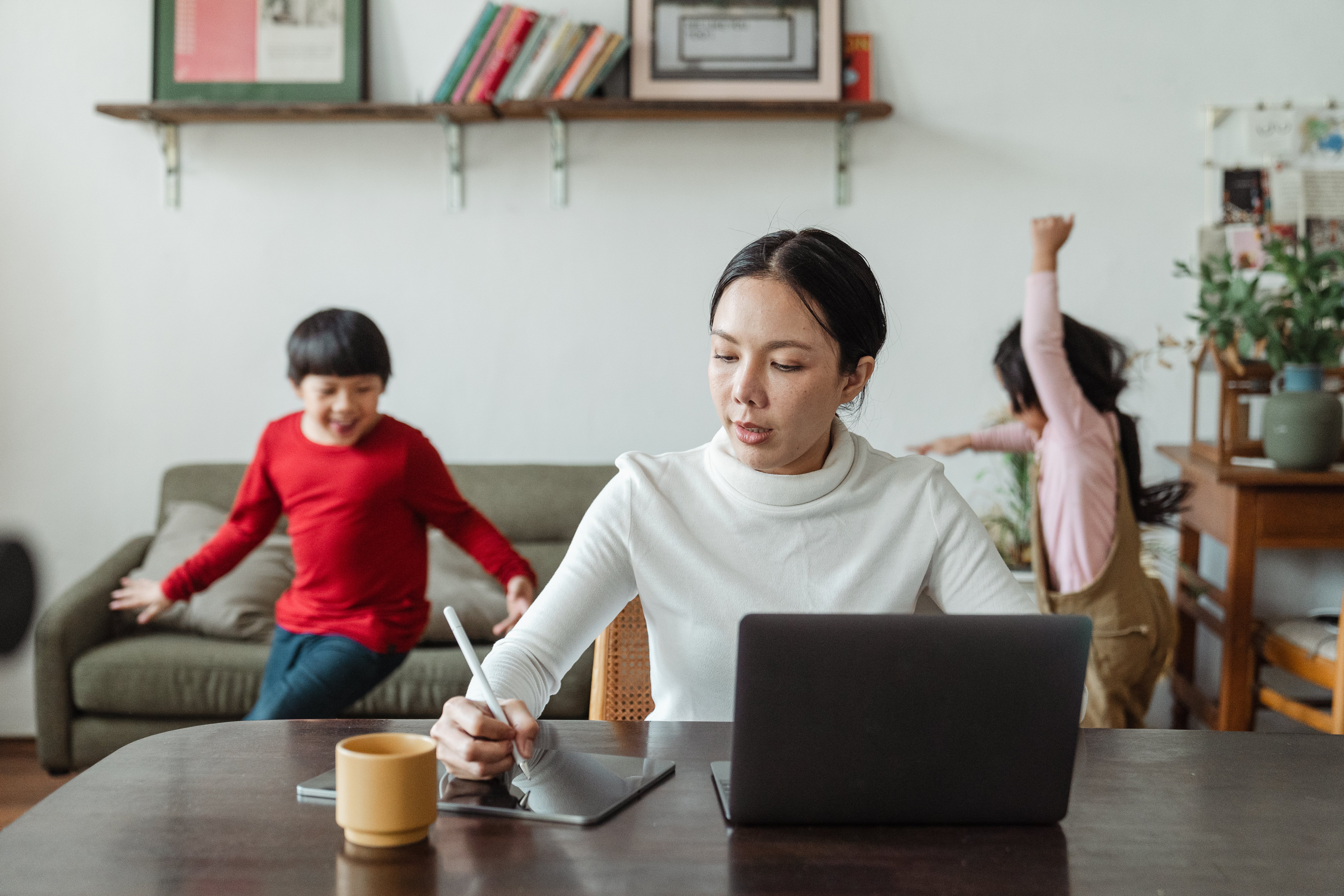 Canva - Busy mom working on laptop and noisy children running around